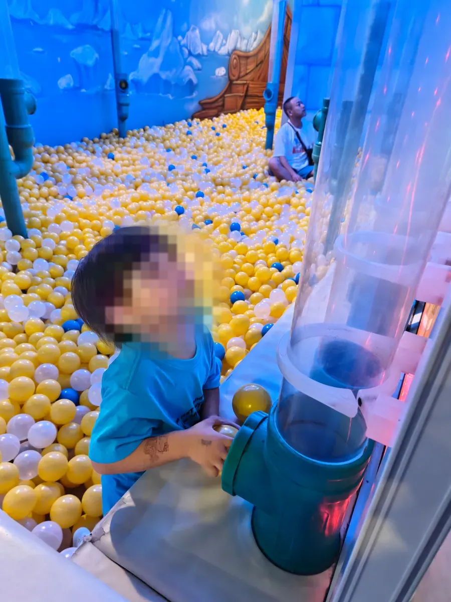 A young child in Amazonia's yellow-and-white snowball pit, beside the ball-vacuum tube.