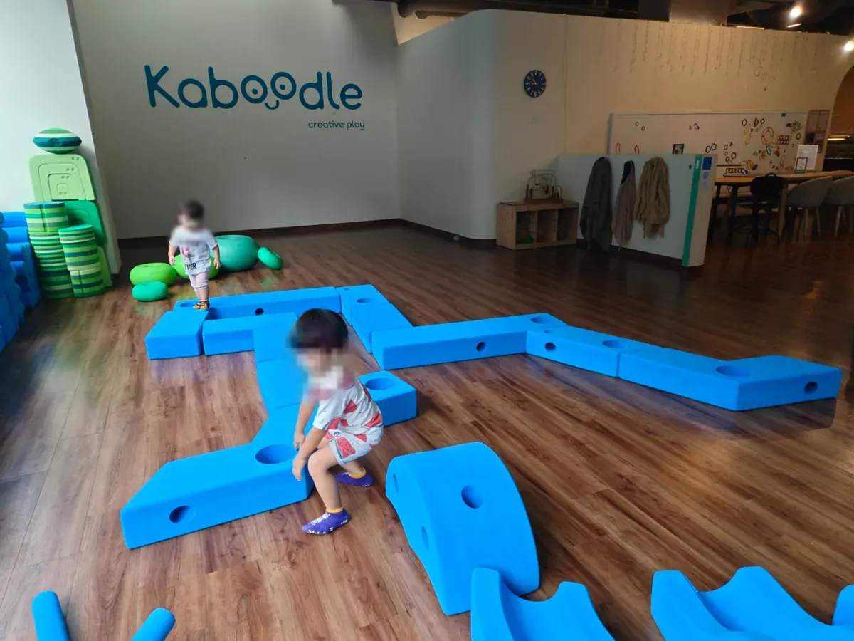 Children building with oversized blue foam blocks at Kaboodle, beneath the venue's logo.