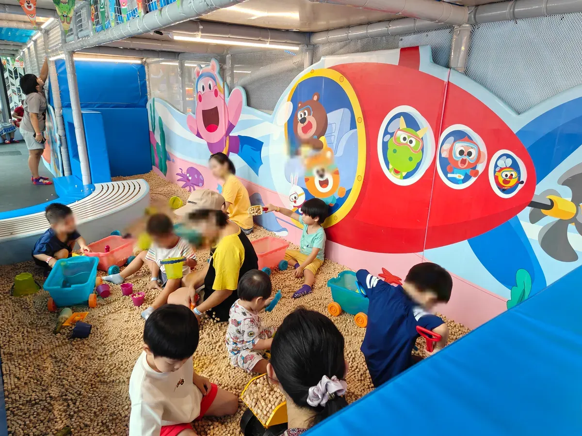Children playing in a kinetic-sand pit beneath a submarine mural at Kiztopia, Woodleigh.