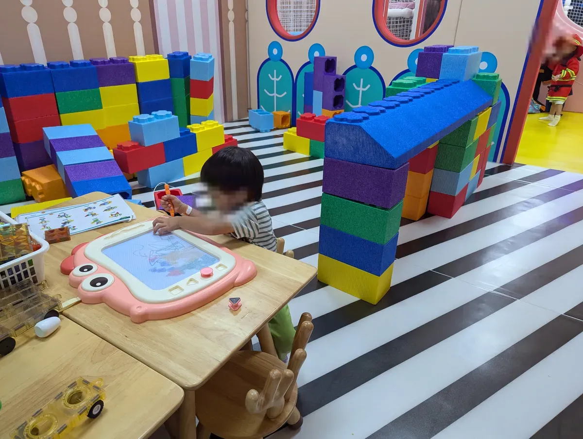 A child drawing at a magnetic board beside giant building blocks at Smigy, United Square.