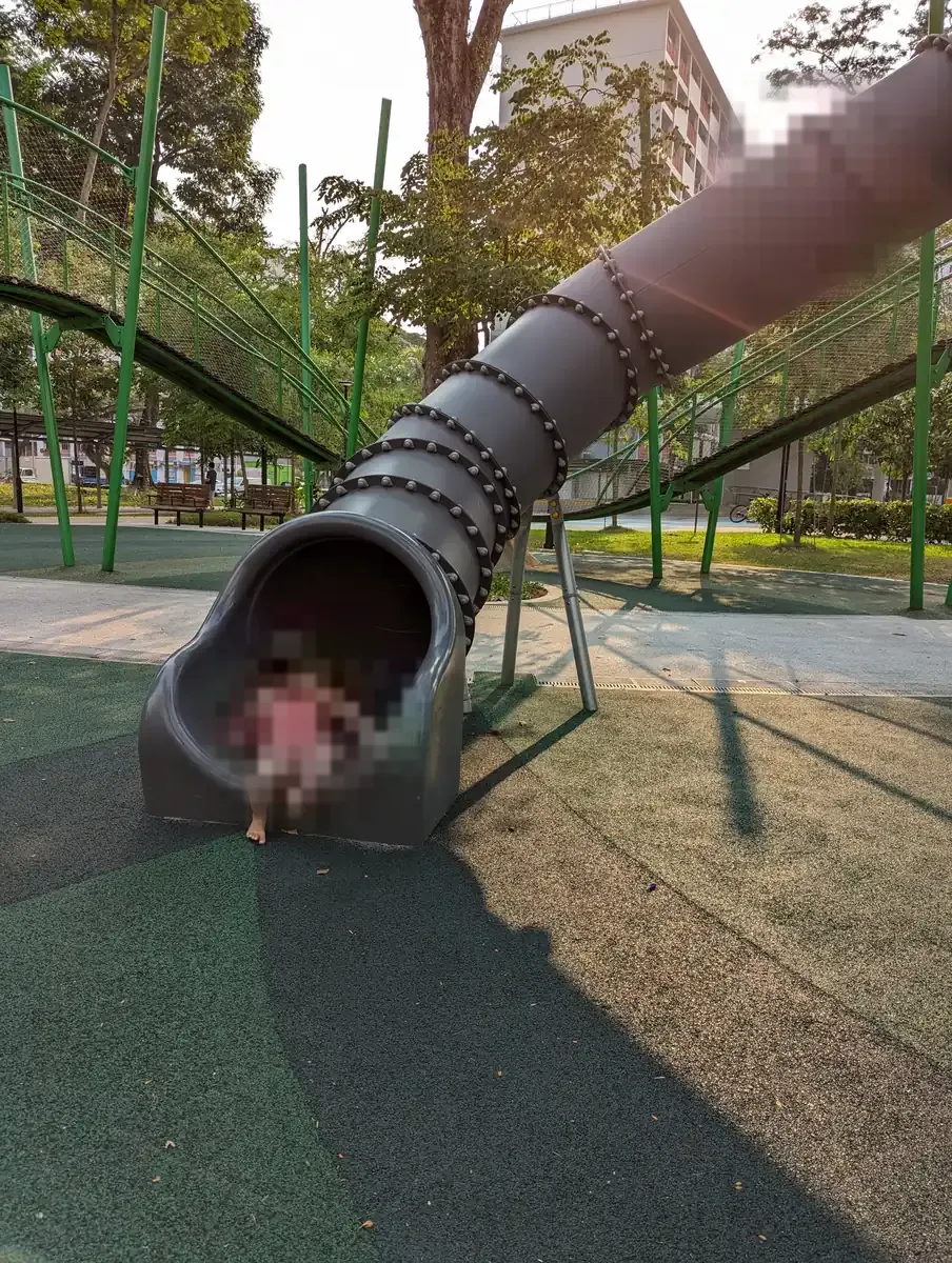 A child at the foot of the grey tunnel slide at Play@Heights, Toa Payoh.